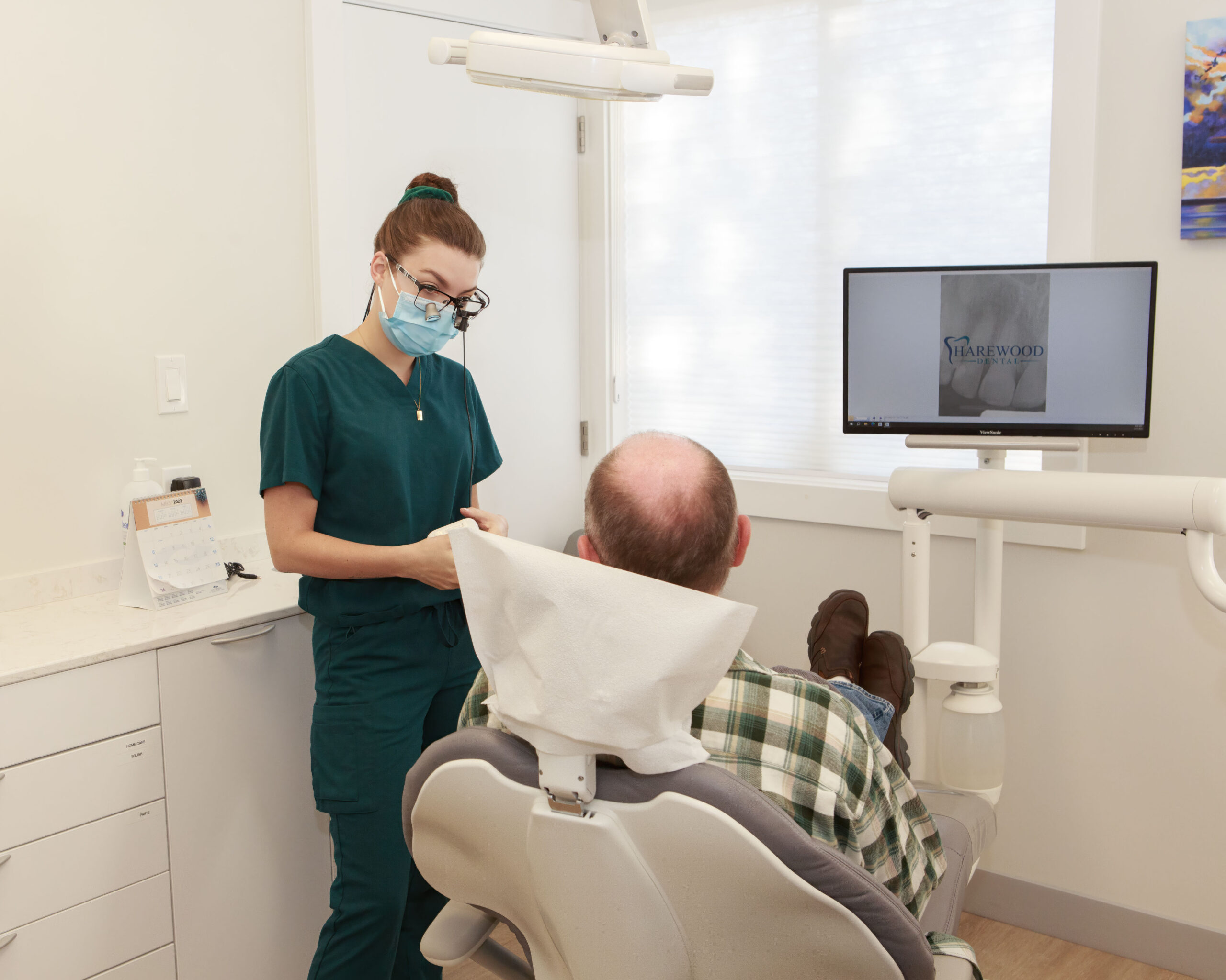 Harewood Dental Clinic a woman in a green scrubs and a mask standing next to a man in a chair
